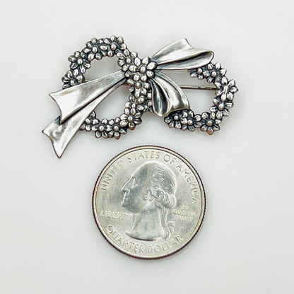 Sterling silver floral wreath bow brooch beside a U.S. quarter showing size.