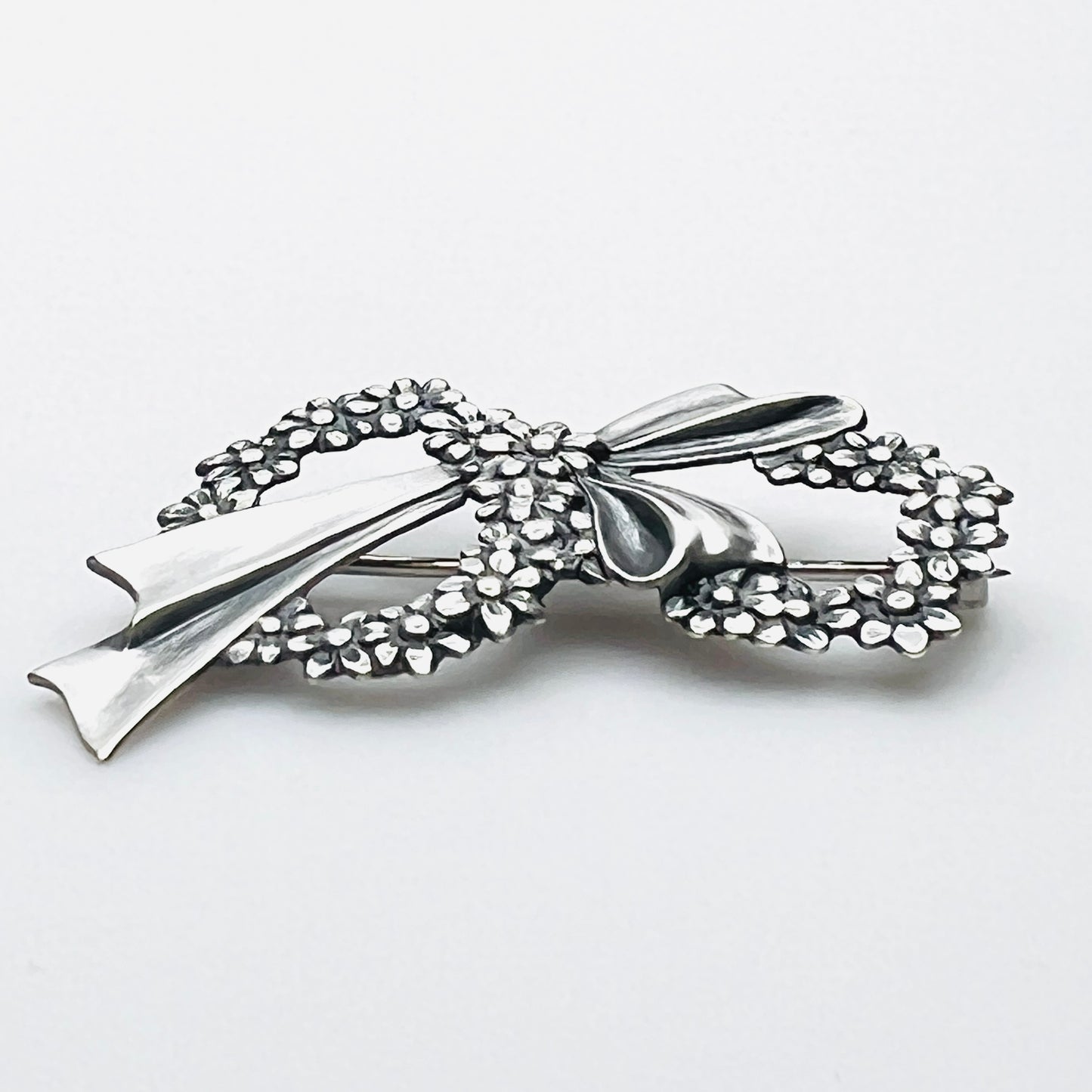 Side profile of vintage sterling silver floral wreath bow brooch with dimensional design.