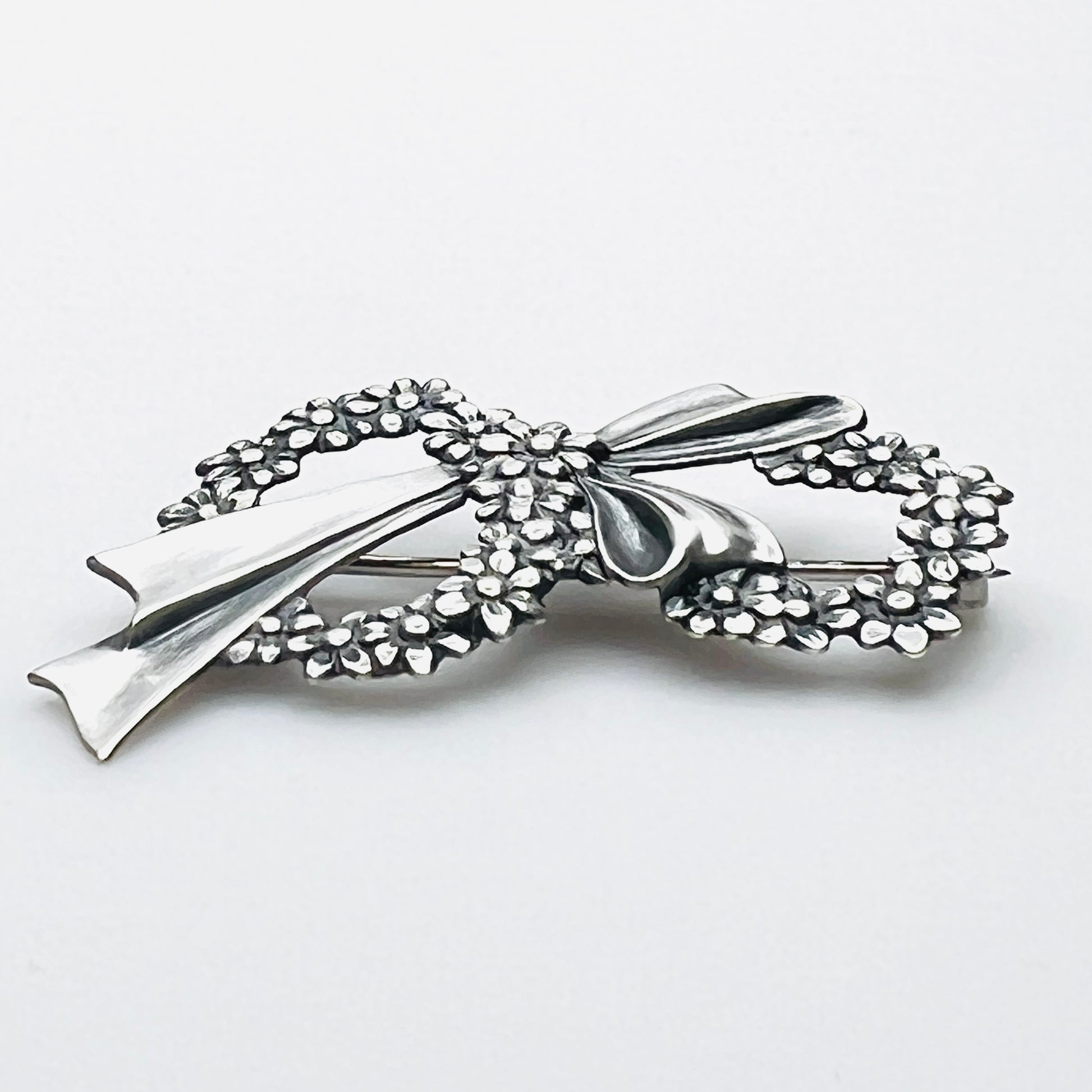 Side profile of vintage sterling silver floral wreath bow brooch with dimensional design.