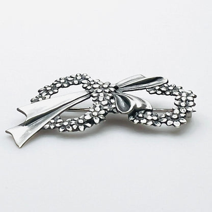 Side profile of vintage sterling silver floral wreath bow brooch with dimensional design.