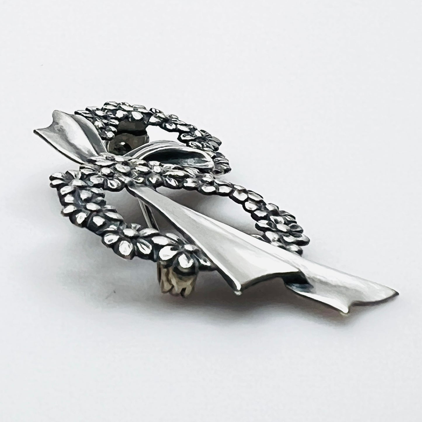 Side profile of vintage sterling silver floral wreath bow brooch with dimensional design.