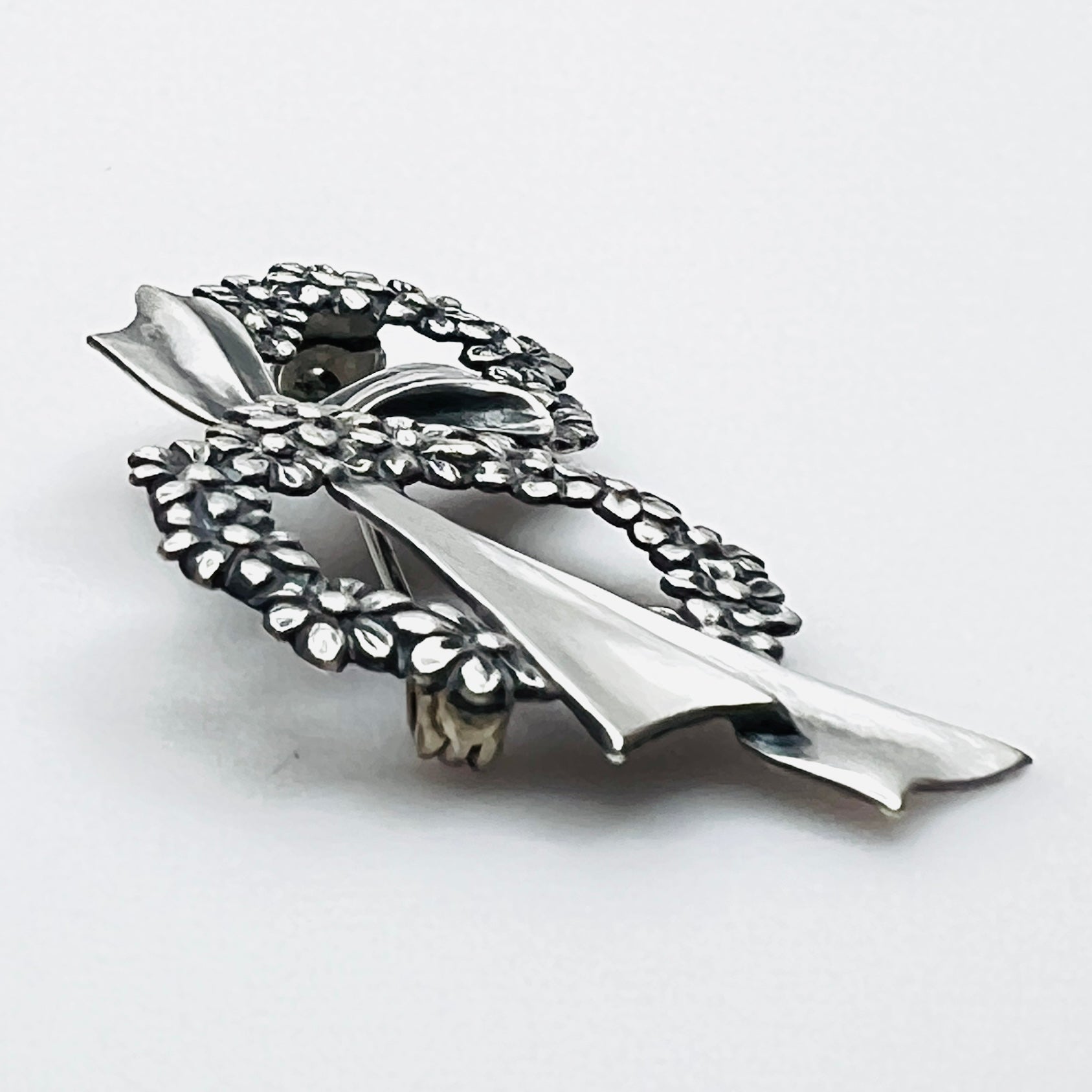 Side profile of vintage sterling silver floral wreath bow brooch with dimensional design.