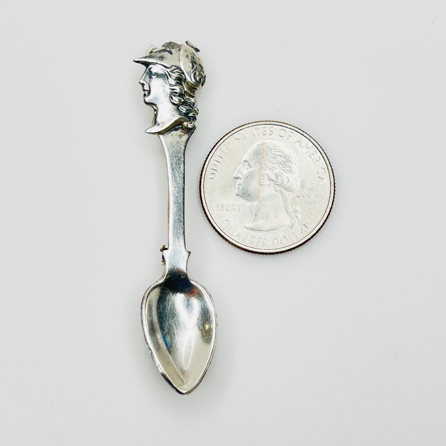 Sterling silver figural spoon pin next to coin for scale