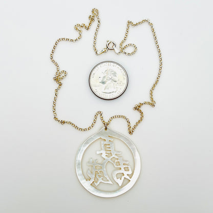 Hand-carved Mother of Pearl Chinese symbol pendant necklace with quarter for size comparison.