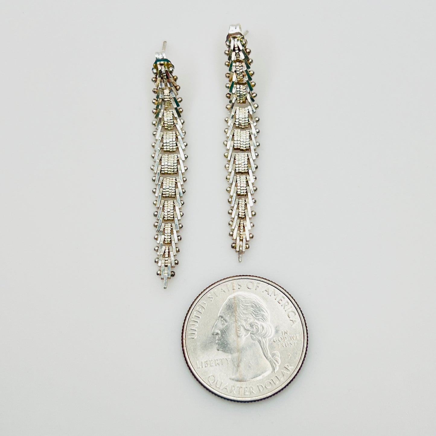 Sterling silver geometric dangle earrings beside quarter for size reference
