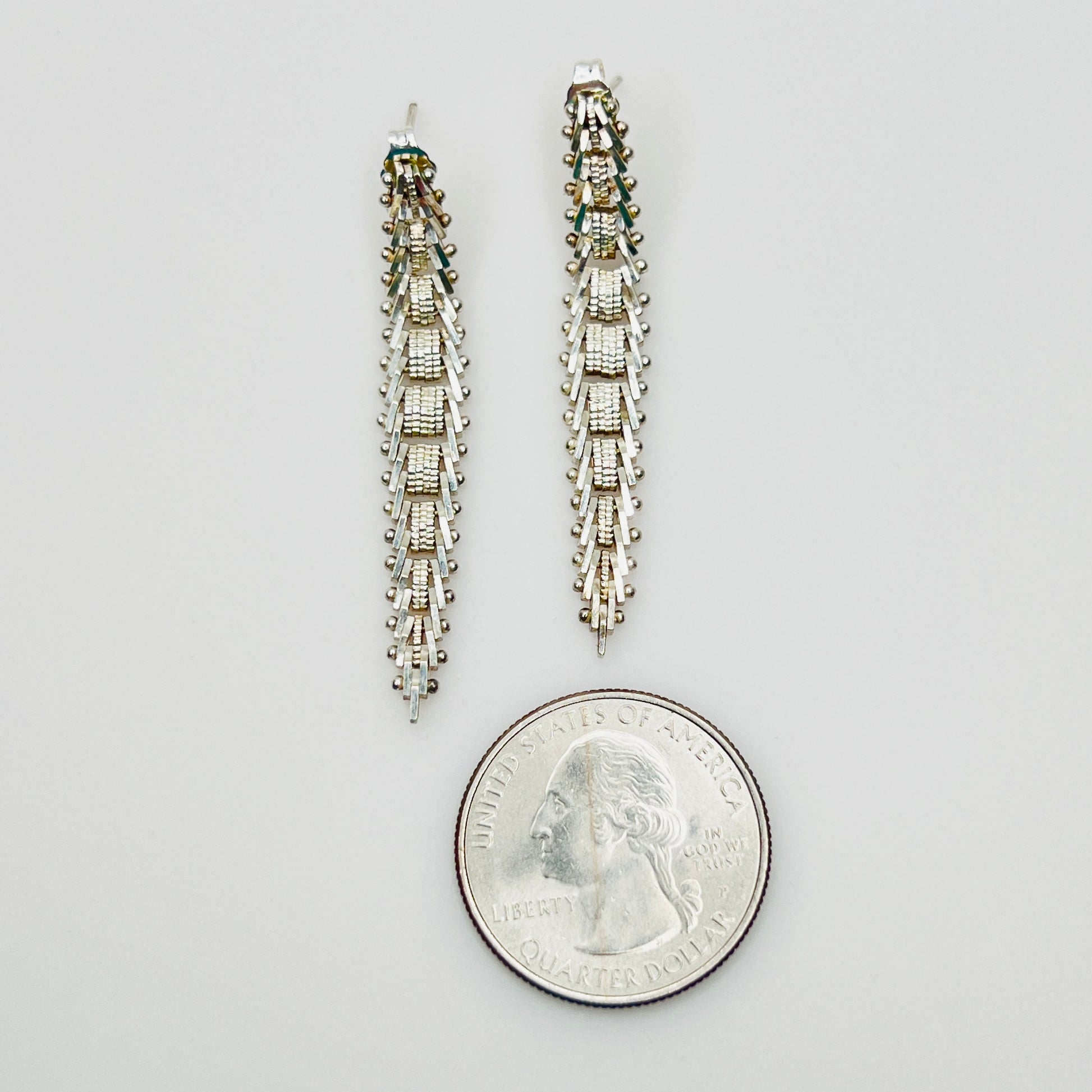 Sterling silver geometric dangle earrings beside quarter for size reference