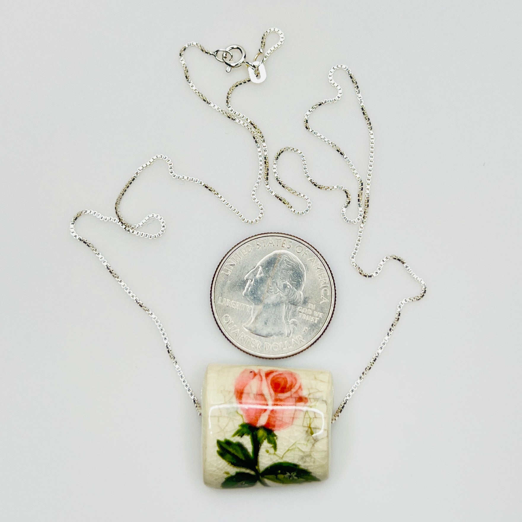 Necklace with a floral pendant next to a quarter for scale on a light gray background