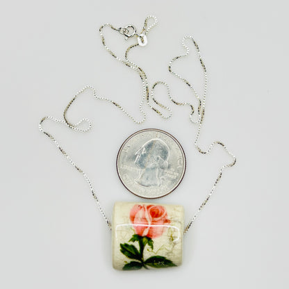 Necklace with a floral pendant next to a quarter for scale on a light gray background