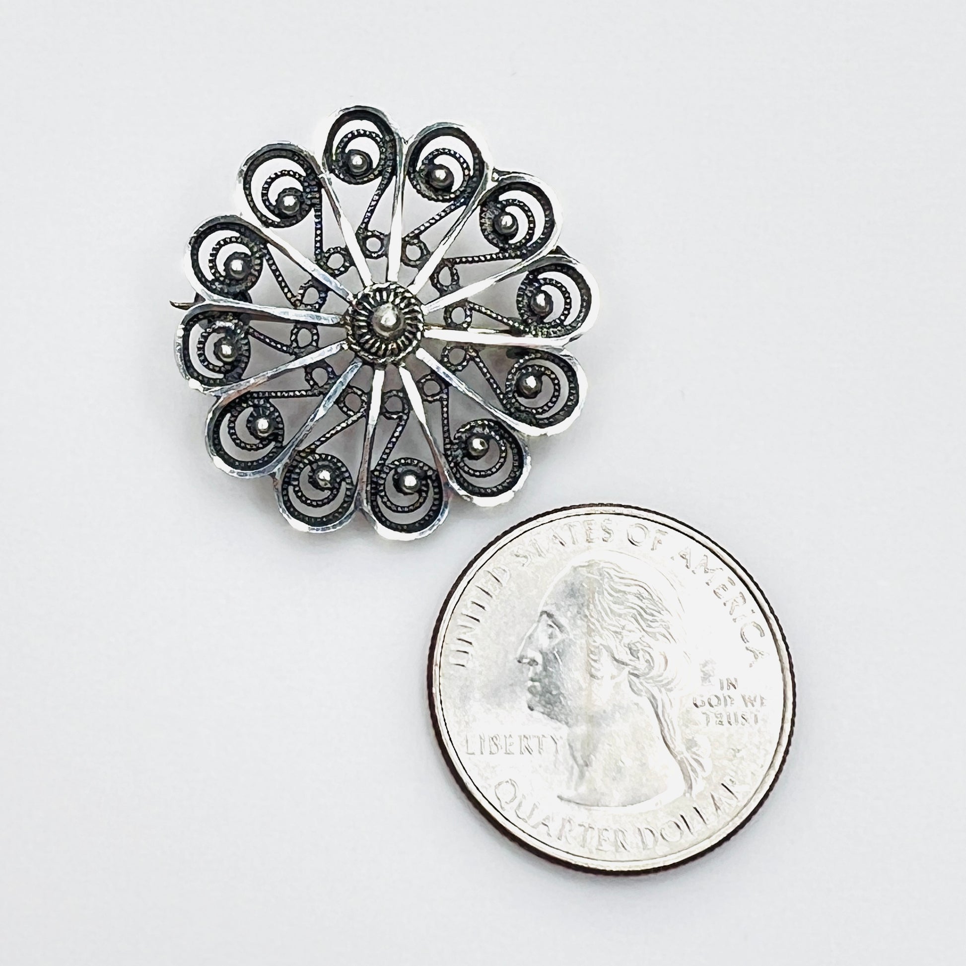 Sterling silver filigree rosette brooch beside a U.S. quarter for scale.