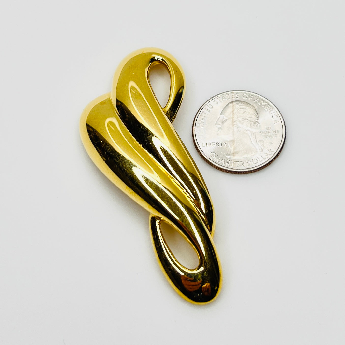 Sculptural gold tone Trifari brooch beside quarter for size comparison