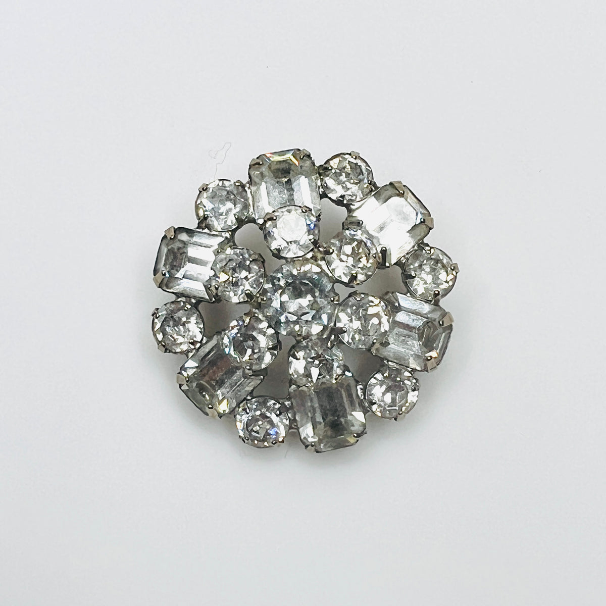 Vintage 1950s signed Weiss clear rhinestone brooch with round and emerald-cut glass crystals in a silver-tone circular cluster setting.