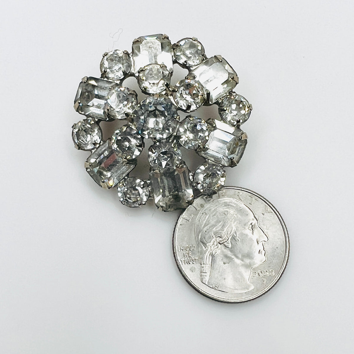 Vintage Weiss crystal brooch beside a quarter for size comparison, showing sparkling clear prong-set rhinestones.