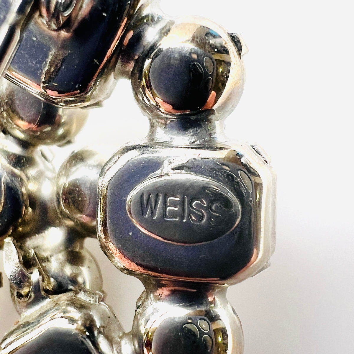 Close-up of oval WEISS maker's signature on reverse of vintage silver-tone rhinestone cluster brooch.