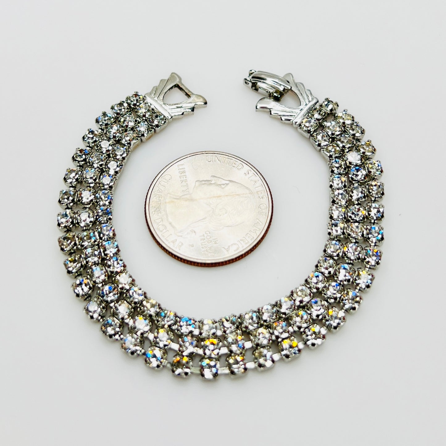 Triple strand Weiss crystal bracelet with silver tone setting beside quarter for scale