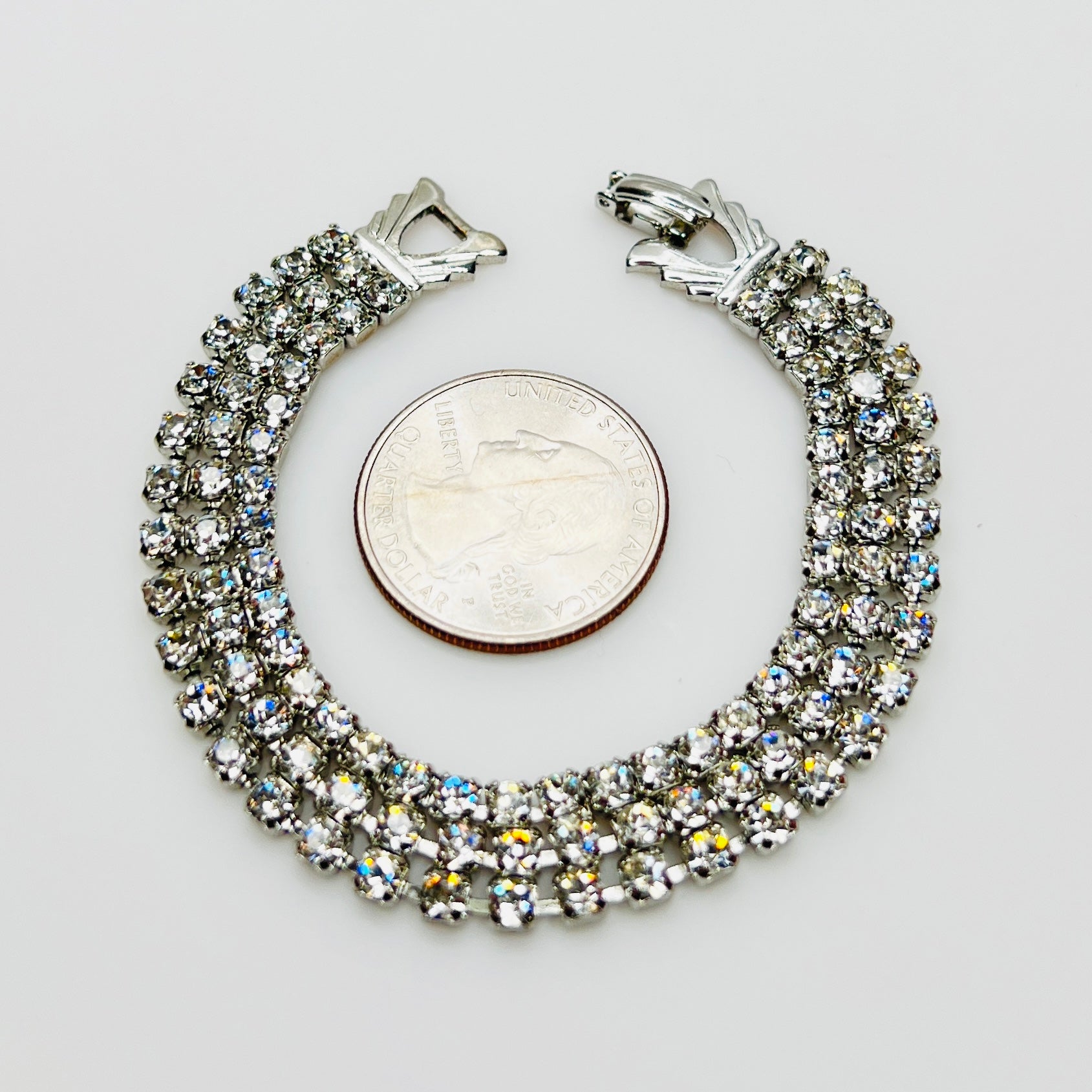 Triple strand Weiss crystal bracelet with silver tone setting beside quarter for scale